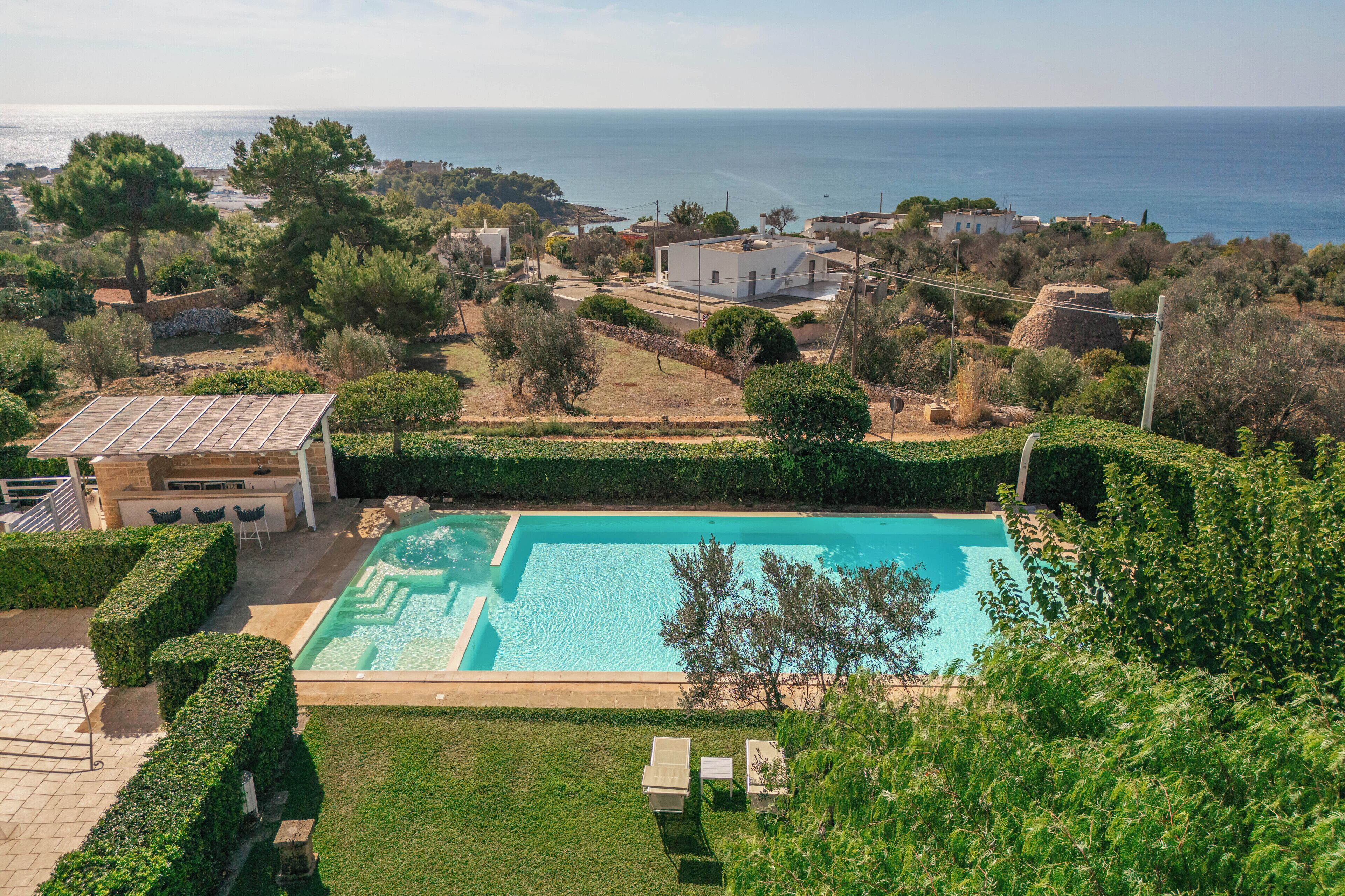 Une grande piscine rectangulaire à l’eau d’un bleu limpide, entourée de haies bien entretenues et d’une pelouse.