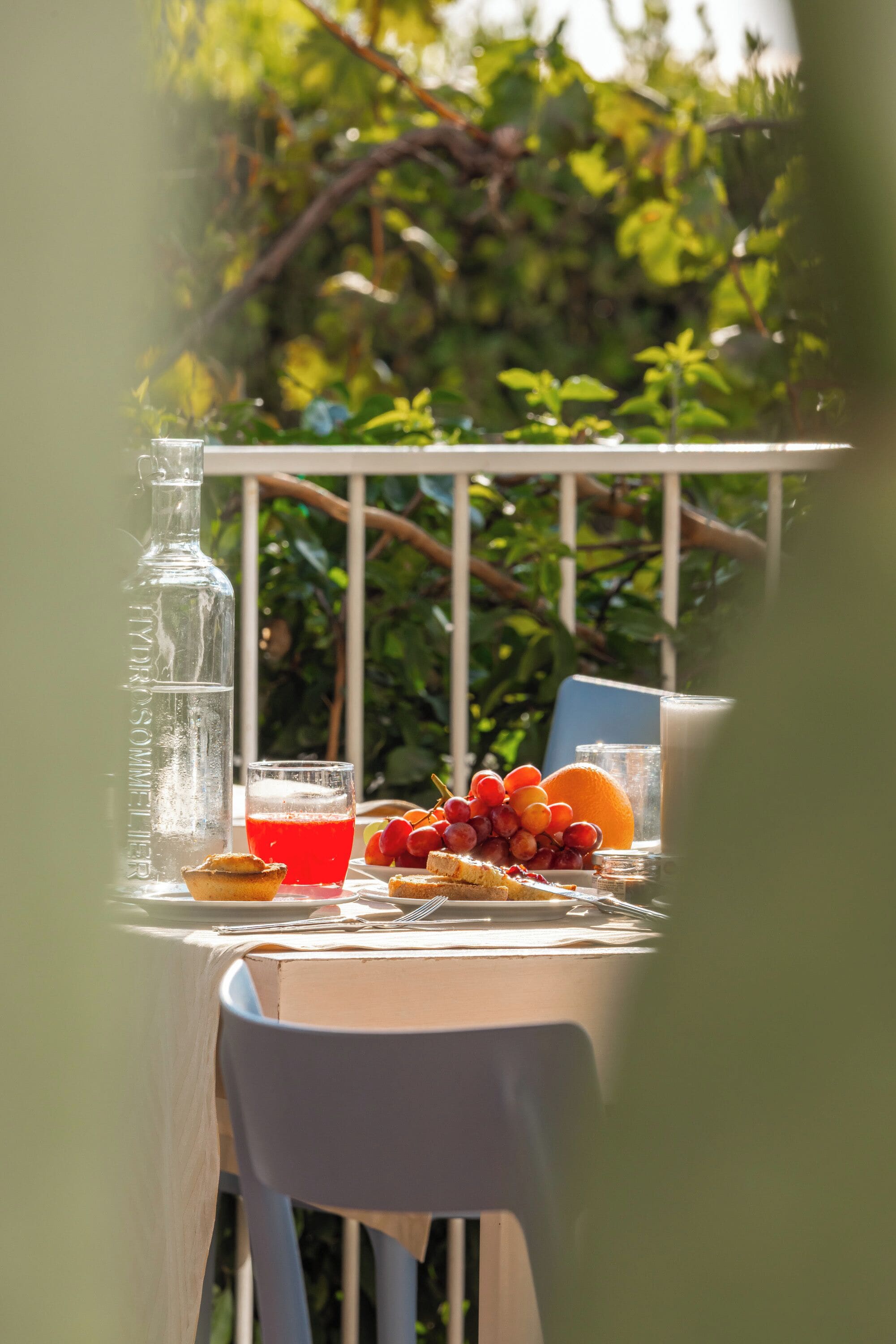 Ein Tisch im Freien mit einer Flasche, einem Glas roter Flüssigkeit, Früchten und einem Muffin.