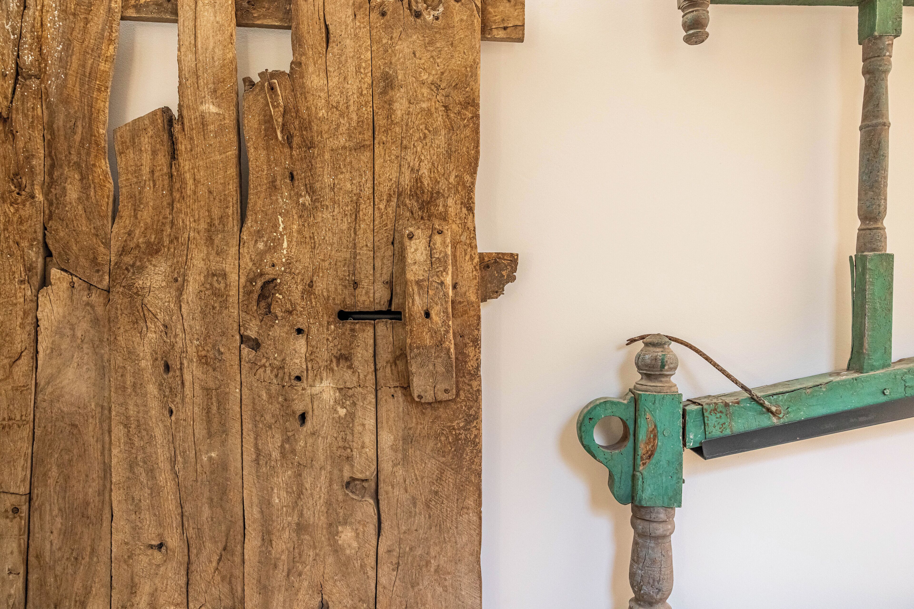 Uma porta de madeira rústica com sinais de uso, uma tranca de metal e uma moldura de metal verde fixada na parede.