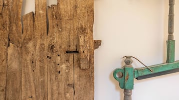Uma porta de madeira rústica com sinais de uso, uma tranca de metal e uma moldura de metal verde fixada na parede.