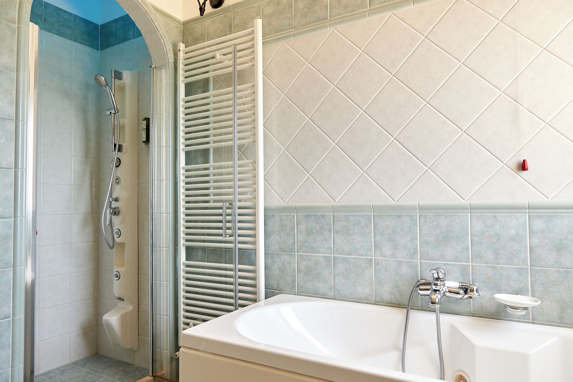 A bathroom with a glass-enclosed shower, a white bathtub, and a tiled wall.