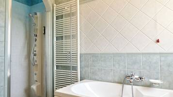 A bathroom with a glass-enclosed shower, a white bathtub, and a tiled wall.