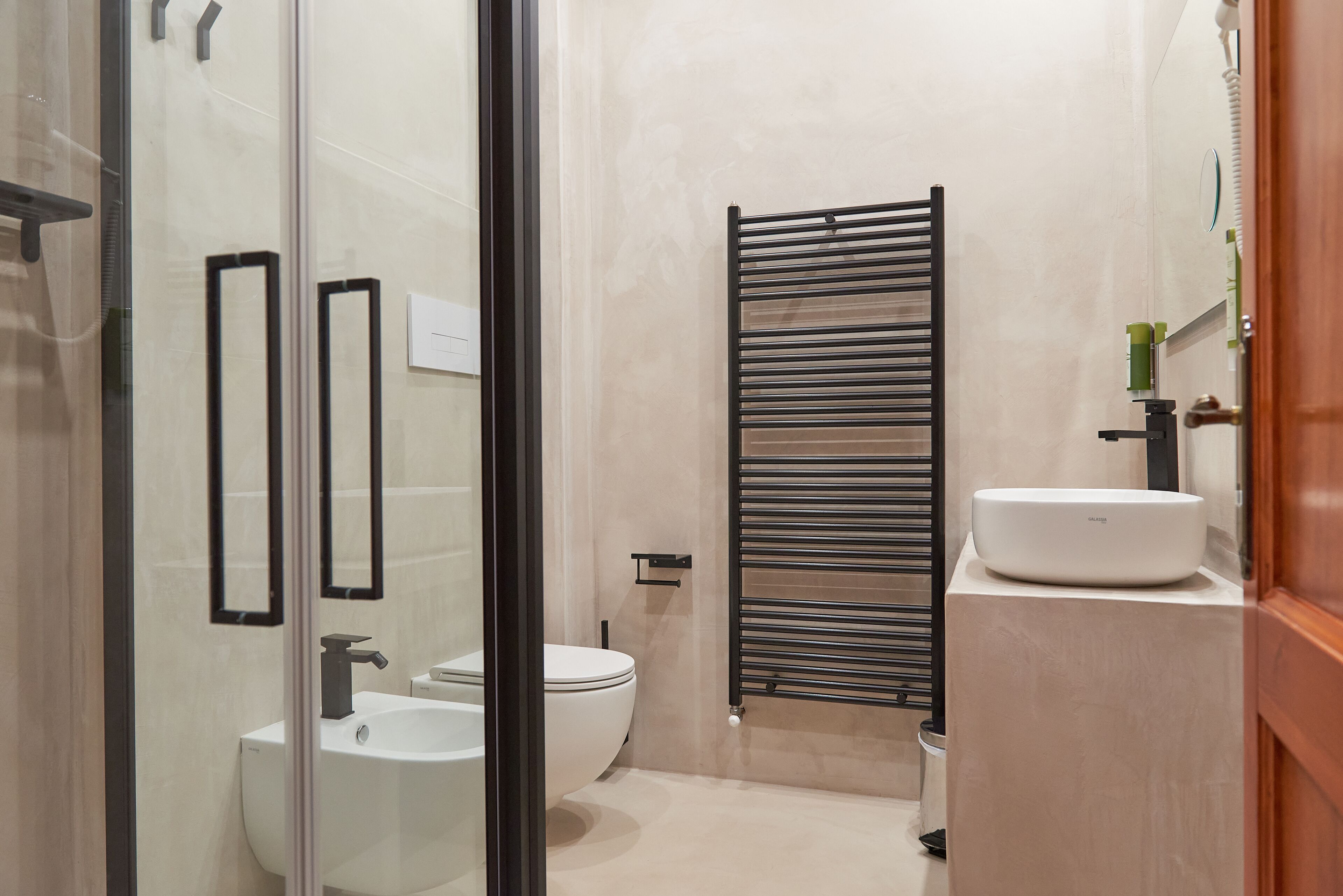 Une salle de bain moderne avec une douche à parois de verre, un lavabo blanc et un porte-serviettes noir.