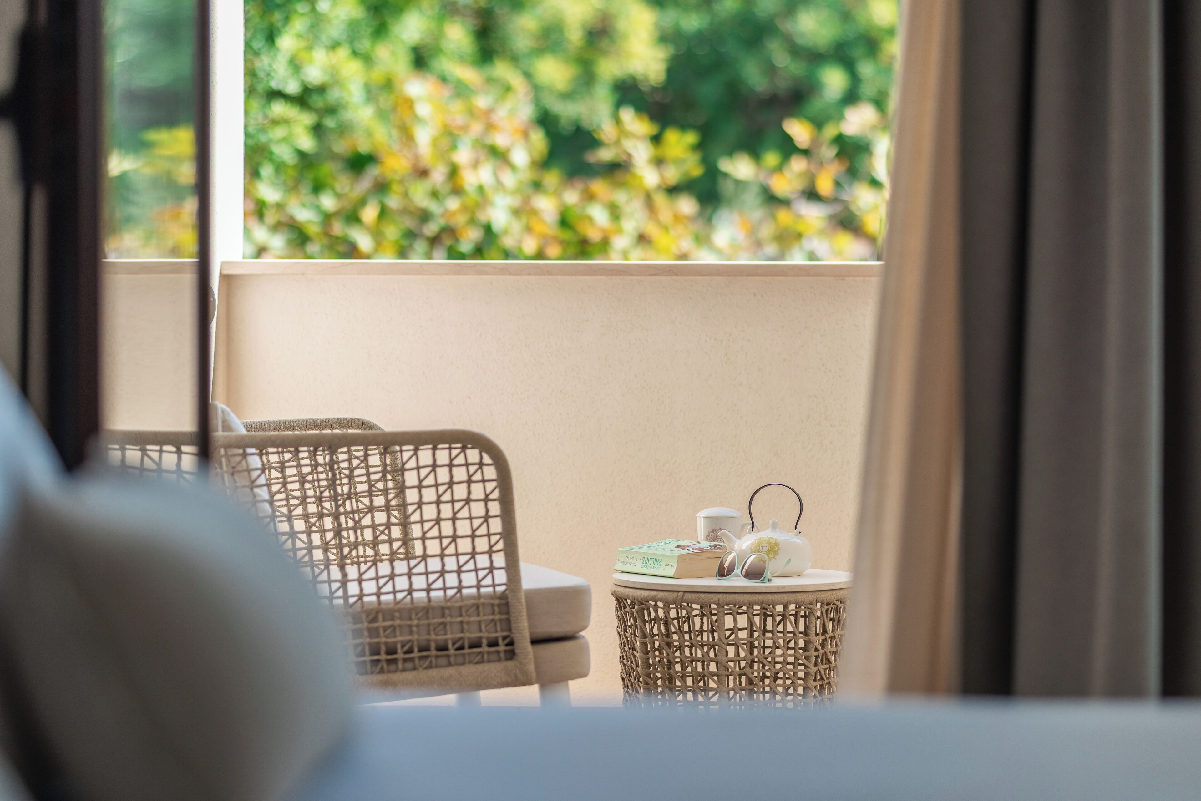 Un balcon agrémenté de meubles en osier, une petite table ronde avec une théière, des tasses et un livre.