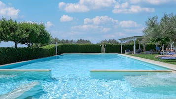 Piscina retangular com água azul cristalina, rodeada por sebes e árvores bem cuidadas.