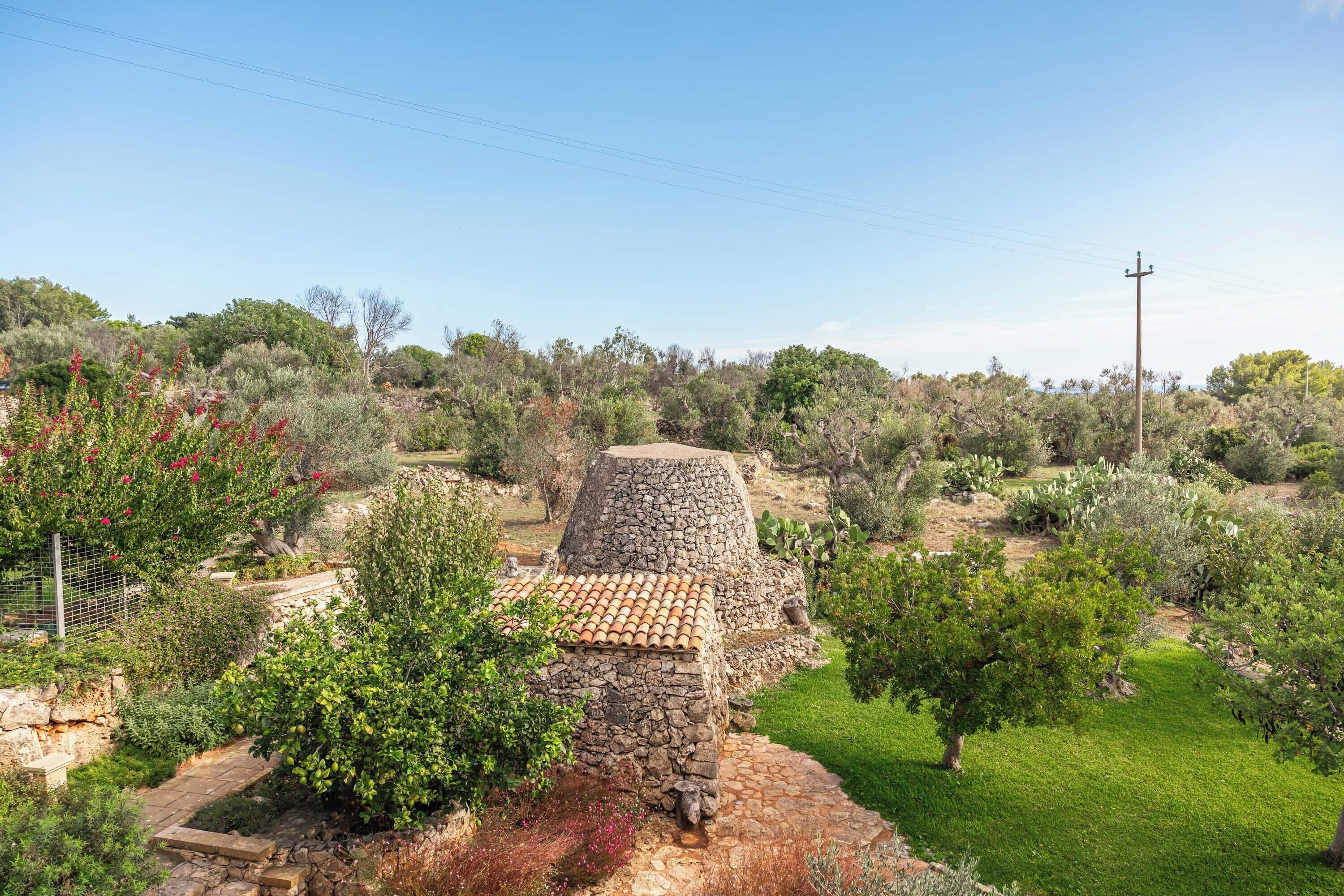 A stone building with a tiled roof surrounded by lush greenery and trees.