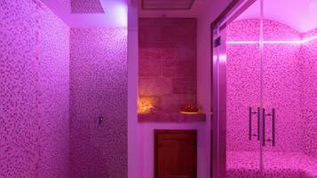 Ett badrum med rosa mosaikplattor, en vägg av natursten, en trädörr och en duschavdelning med glasväggar.