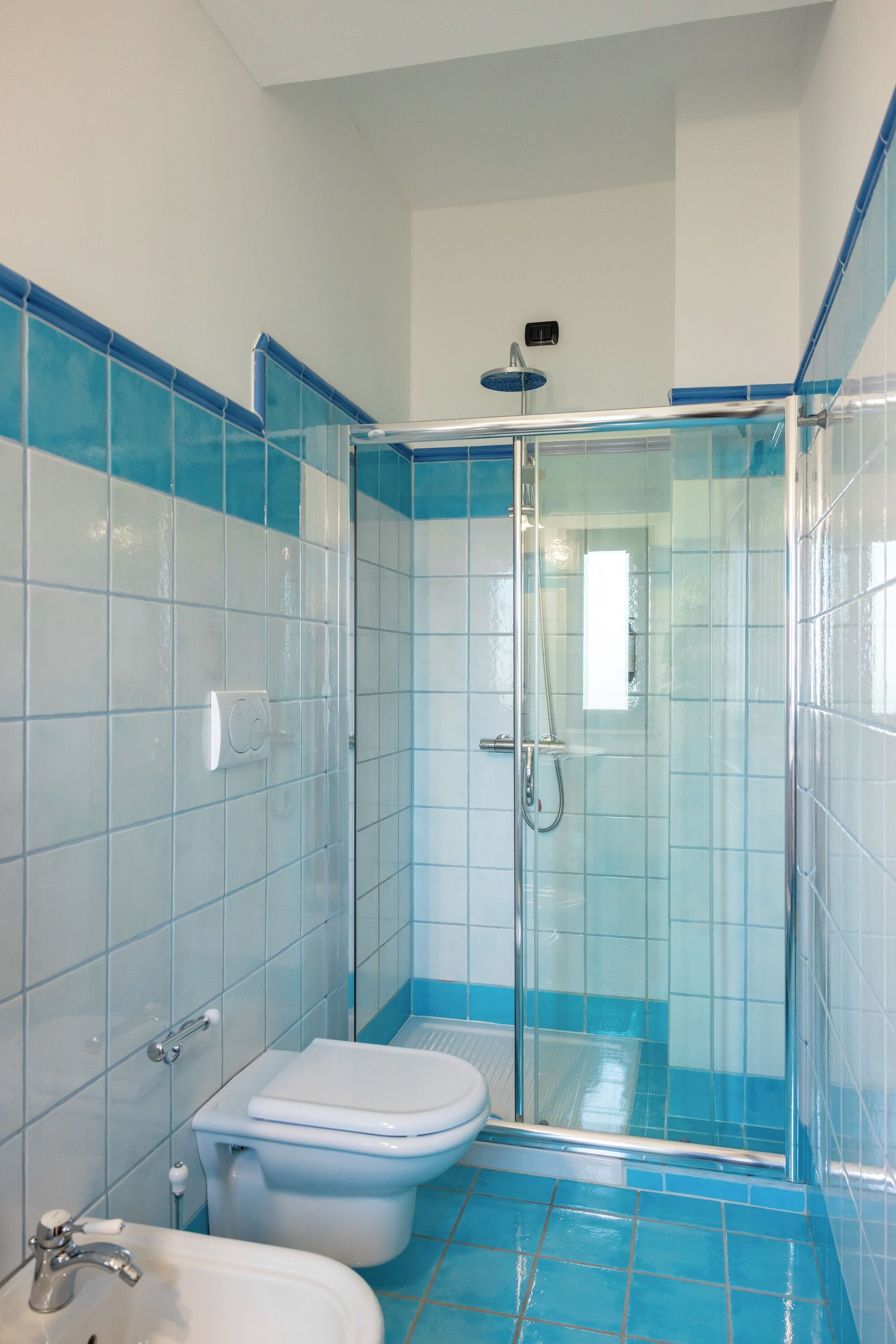 A bathroom with a glass-enclosed shower, a toilet, and a sink.