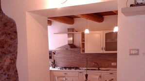 Una cocina con armarios blancos, una estufa y una zona de comedor con sillas blancas.