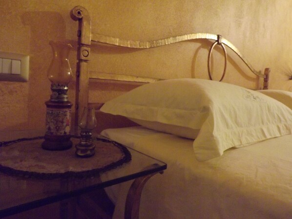 A bed with white bedding, a bedside table with a lamp, and a wall-mounted light fixture.