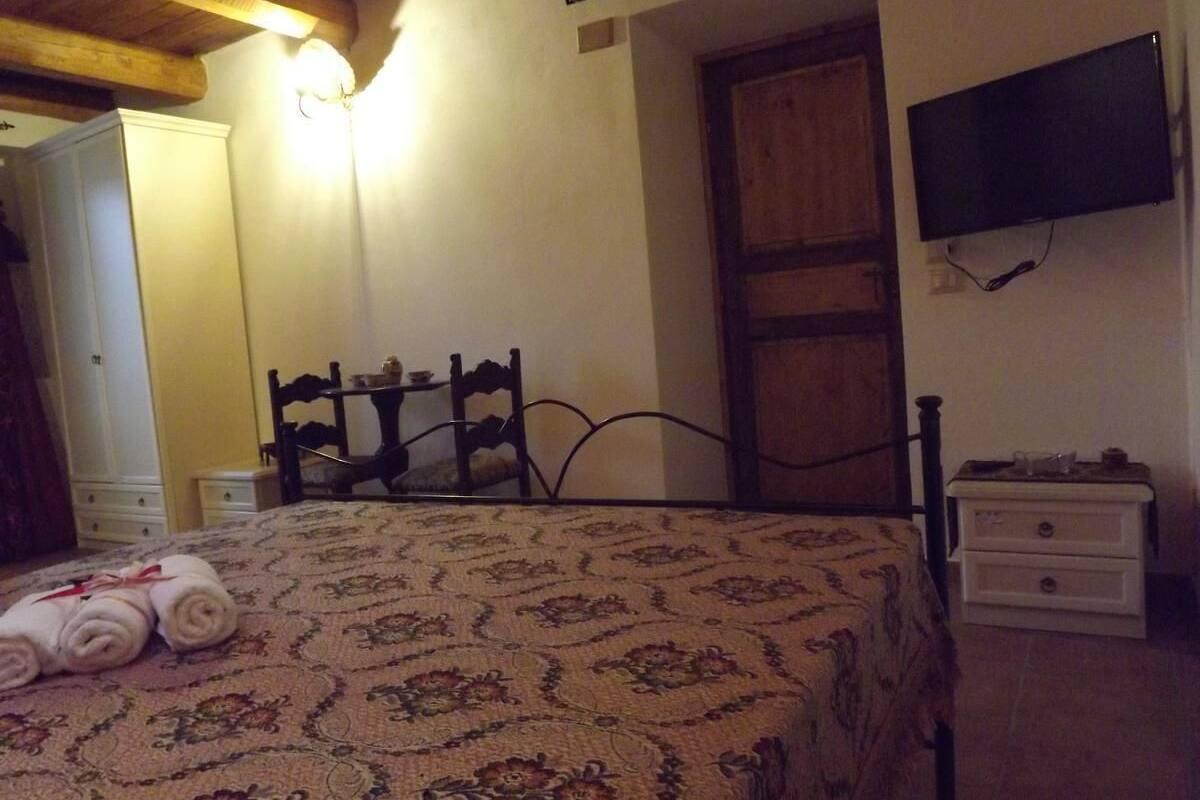 Una habitación con una cama, una silla de madera, una mesita de noche, un televisor montado en la pared y un armario.