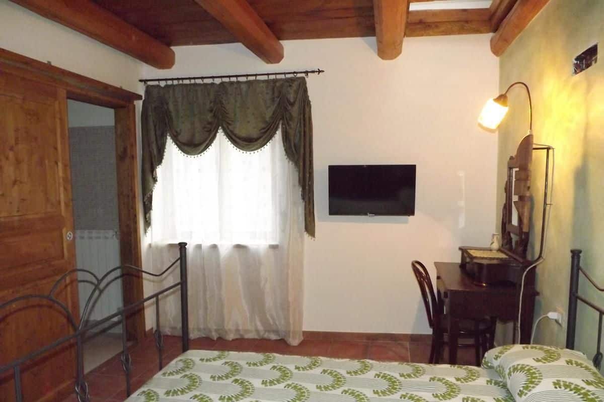 Un dormitorio con cama, escritorio, silla, televisor y lámpara.