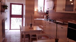 Una cocina con armarios blancos, una mesa de comedor, sillas, una estufa y lámparas colgantes.