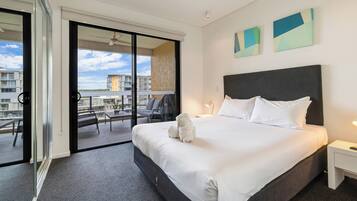 A hotel room with a large bed, a nightstand, a window with a view of the city, and a sliding glass door to an outdoor area.