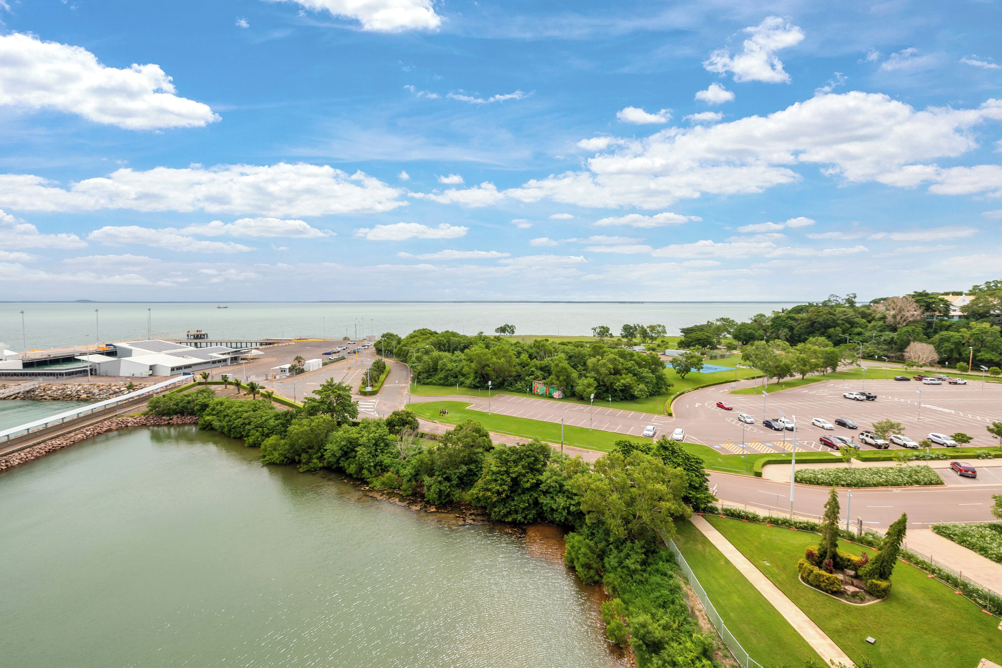 An aerial view of a coastal area with a parking lot, a marina, and lush greenery.