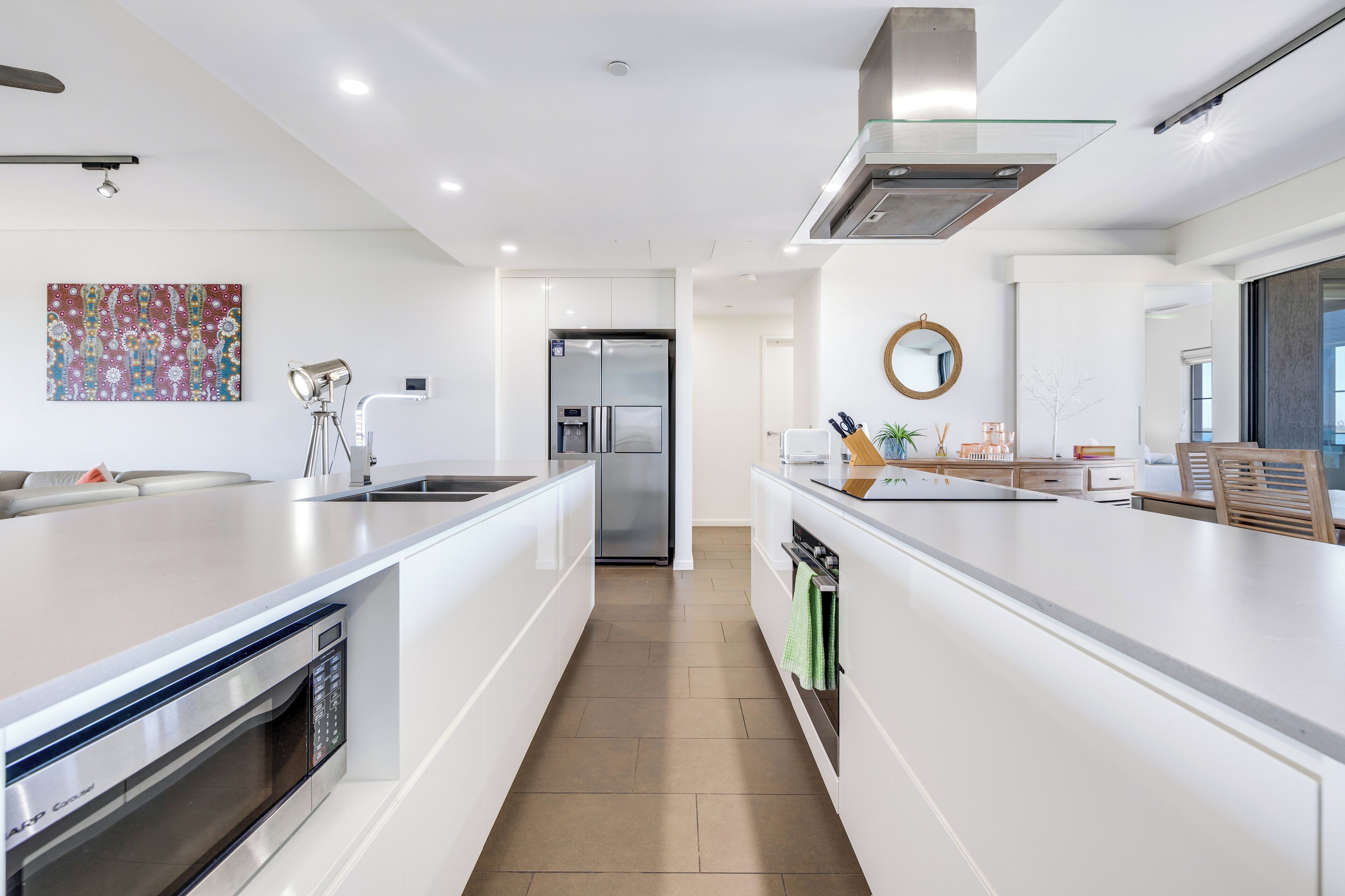 A modern kitchen with white cabinetry, a built-in oven, a stainless steel refrigerator, and a large island with a sink.