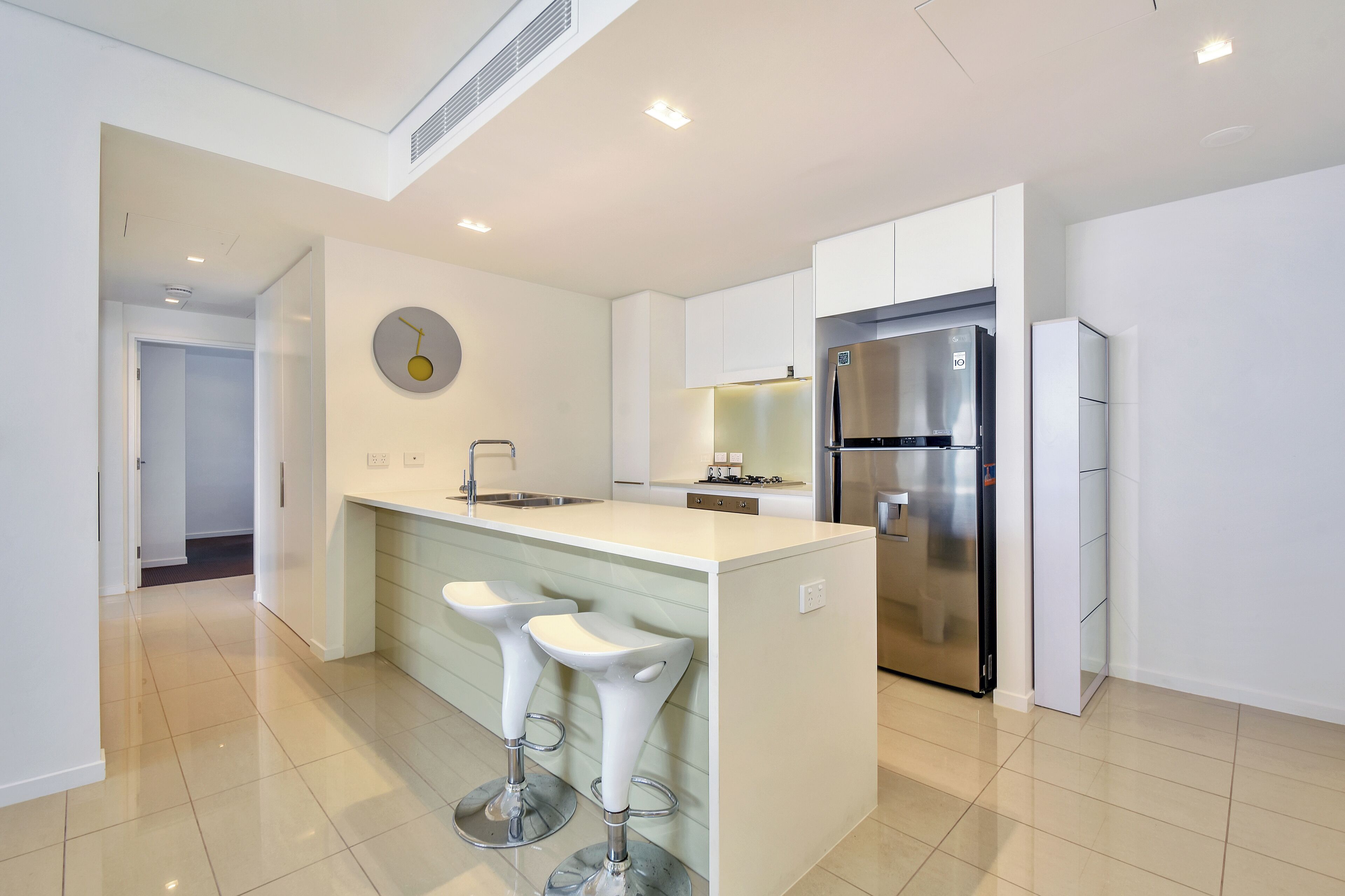 A modern kitchen with white cabinetry, a stainless steel refrigerator, and a central island with two bar stools.