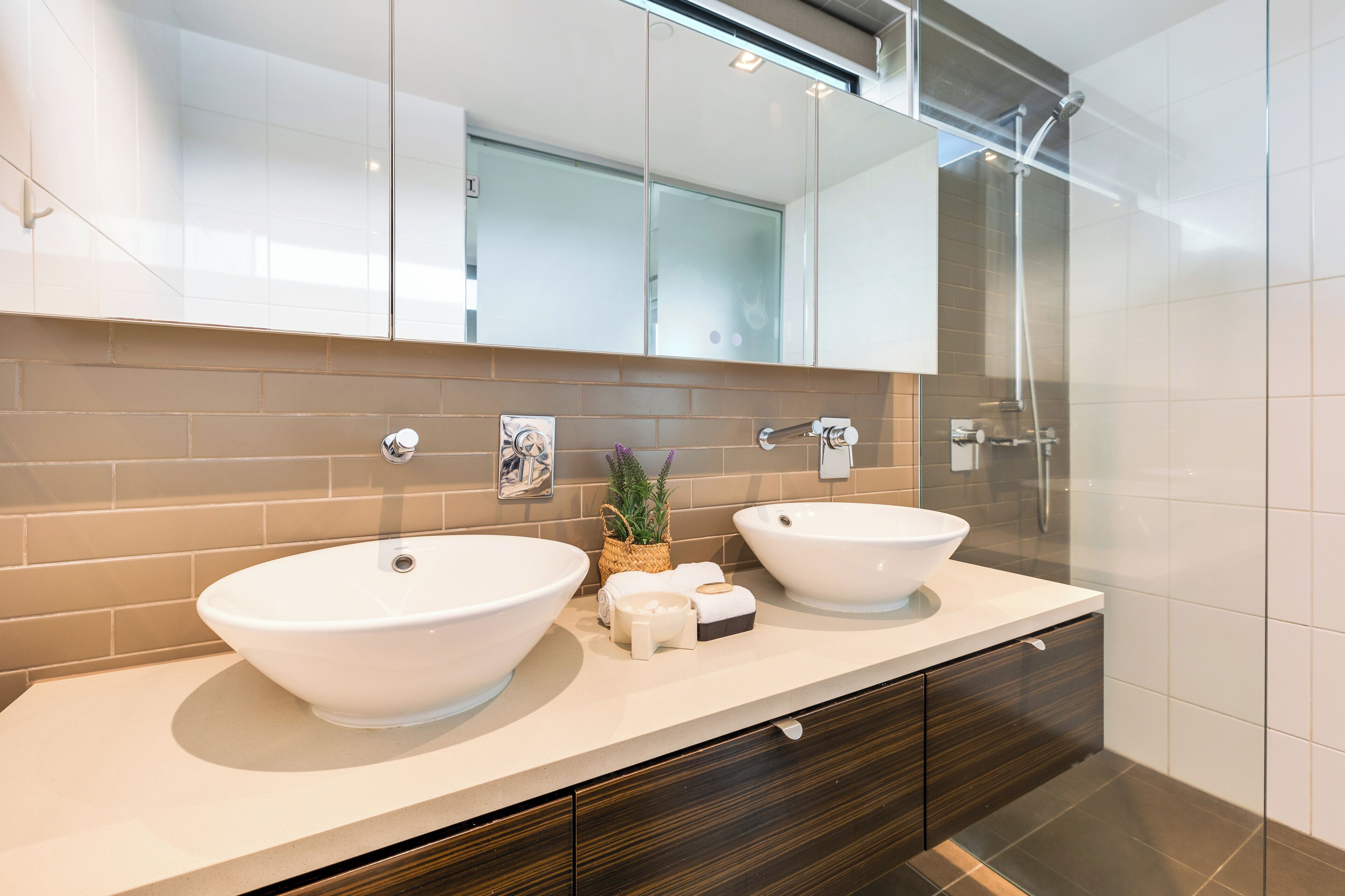 Un baño moderno con dos lavamanos grandes de color blanco, un espejo arriba y una zona de ducha.