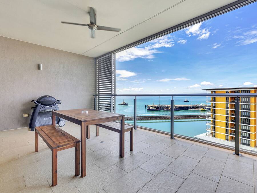 A balcony with a view of the sea, a grill, and a table.