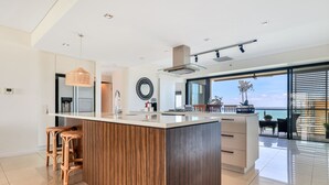 Una cocina moderna con una isla central, taburetes de bar, un amplio ventanal con vistas y un comedor con mesa y sillas.
