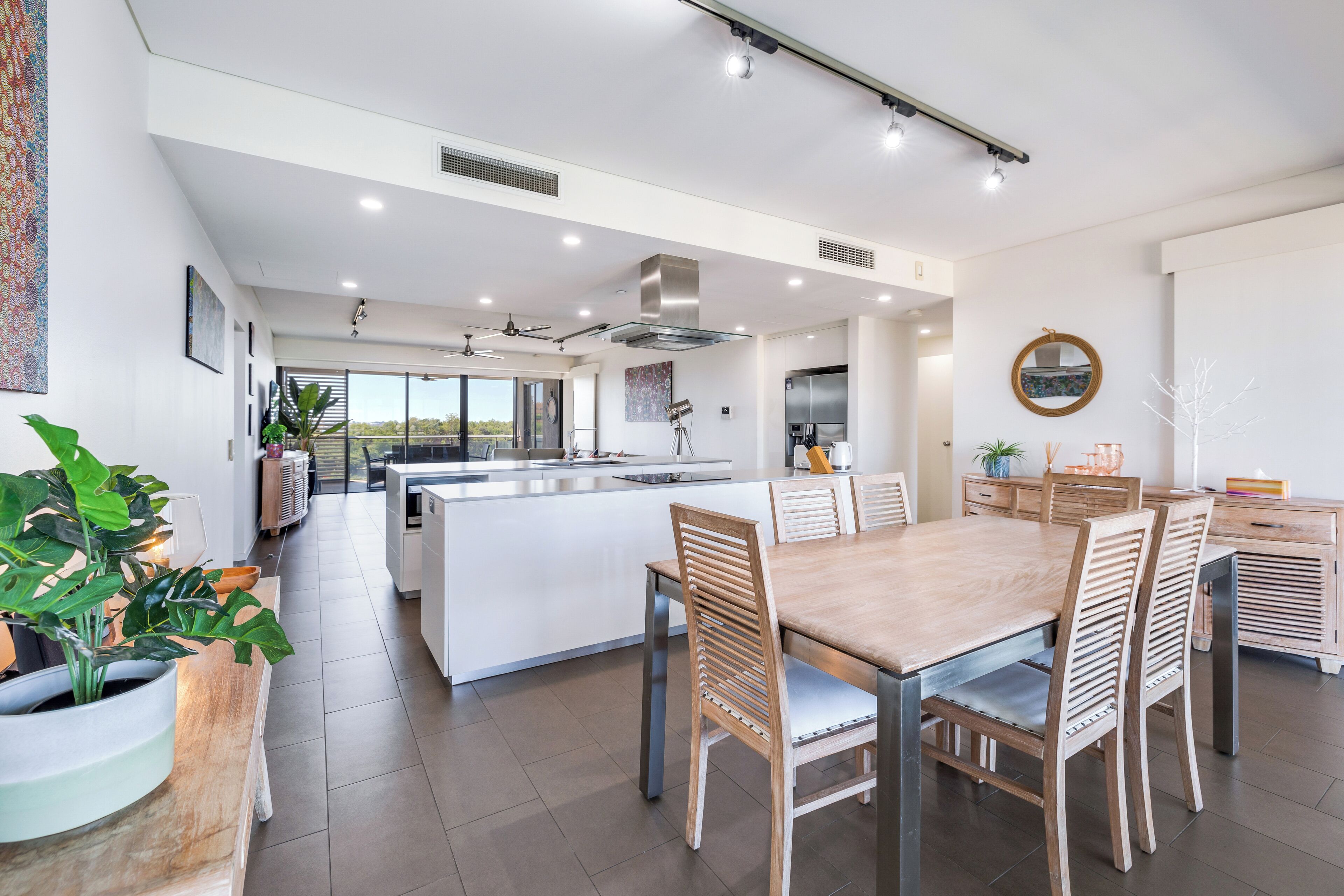 Une cuisine moderne dotée d’un îlot central, de meubles blancs et d’un coin repas avec des chaises en bois.