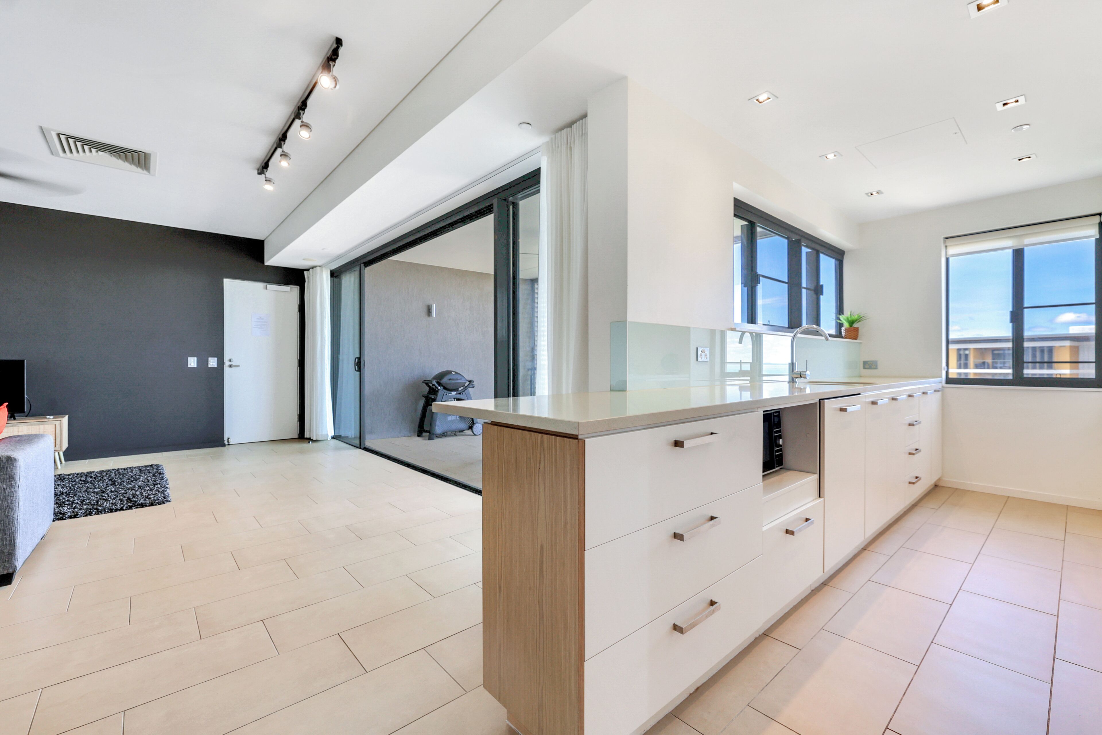 A modern kitchen with a large island, a sliding glass door leading to a balcony, and a view of the cityscape.