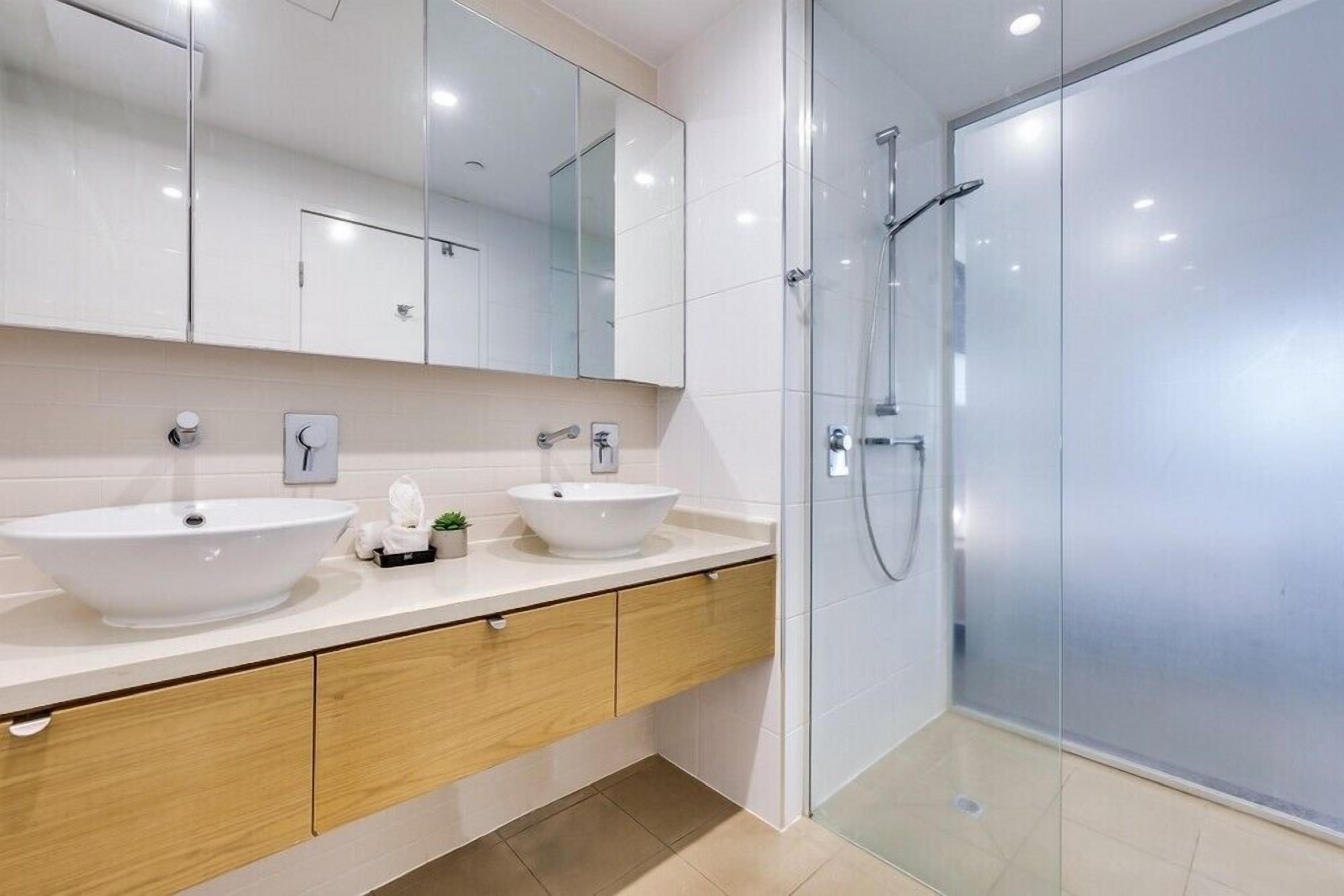 Een moderne badkamer met twee wasbakken, een grote spiegel en een douche met glazen wanden.