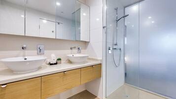 Een moderne badkamer met twee wasbakken, een grote spiegel en een douche met glazen wanden.