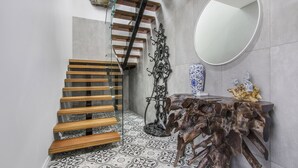 A modern staircase with wooden steps and glass railings, a decorative metal sculpture, a round mirror, and a wooden table with a unique design. - The Apartment, Metung (Metung)