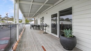 A covered outdoor area with a wooden deck, outdoor seating, and large potted plants. - The Apartment, Metung (Metung)
