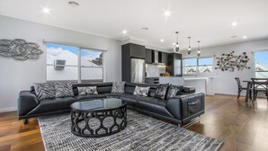 A modern living room with a black leather sectional sofa, a glass coffee table, and a patterned rug. - The Apartment, Metung (Metung)