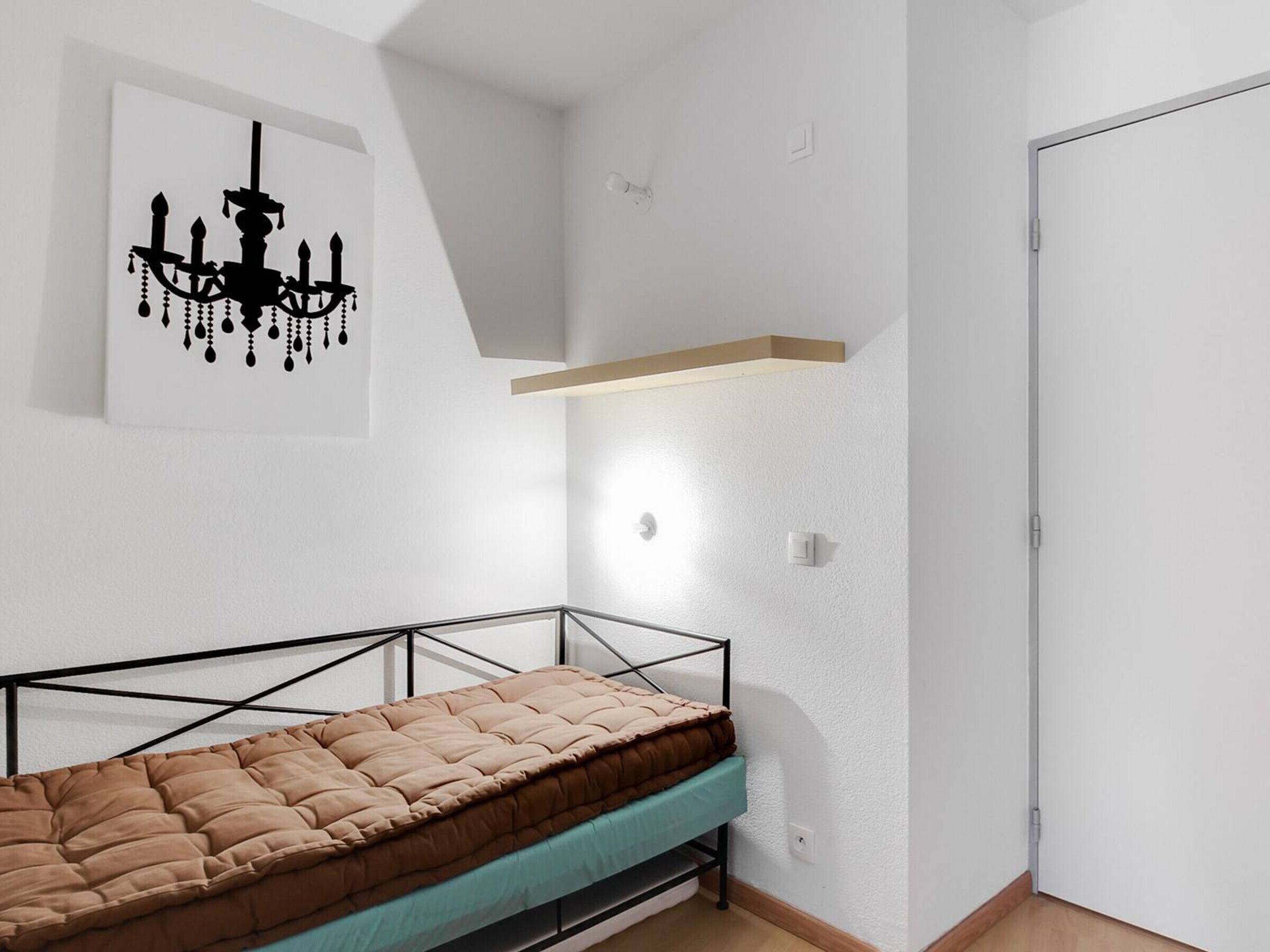 Ein kleines, modernes Schlafzimmer mit Etagenbett, weißer Wand, einer Chandelüster und einer Tür.