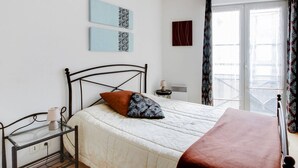 Un dormitorio con cama, mesita de noche, lámpara y ventana con cortinas.