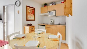 Cocina compacta con microondas, lavamanos y armarios de madera. Hay una mesa de comedor con sillas y un cuadro en la pared.