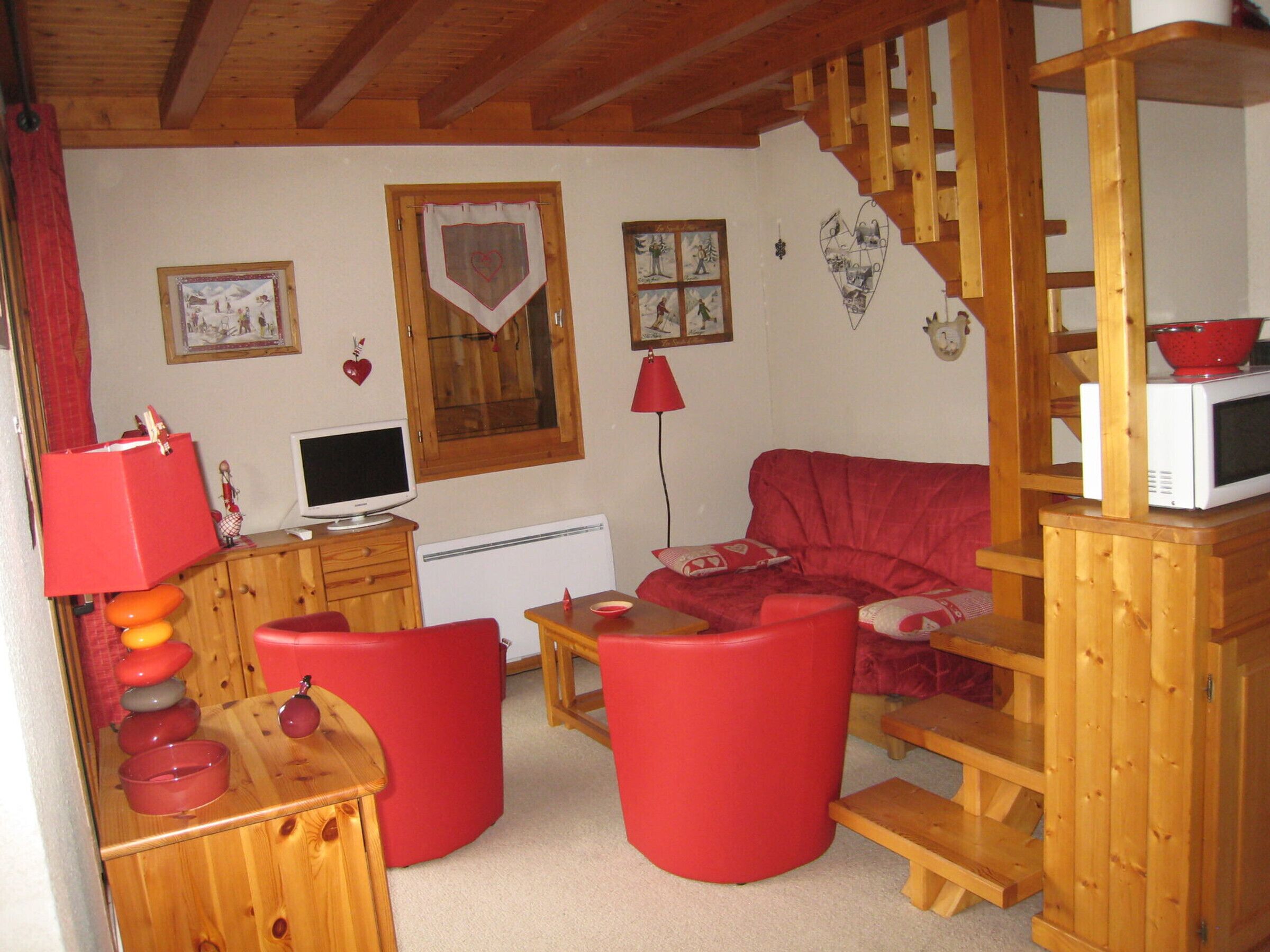 Un salon chaleureux avec un canapé rouge, des meubles en bois, une télévision et un four à micro-ondes posé sur un meuble en bois.