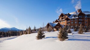 Un gran lodge con varias edificaciones, rodeado de terreno y árboles cubiertos de nieve, y montañas al fondo.