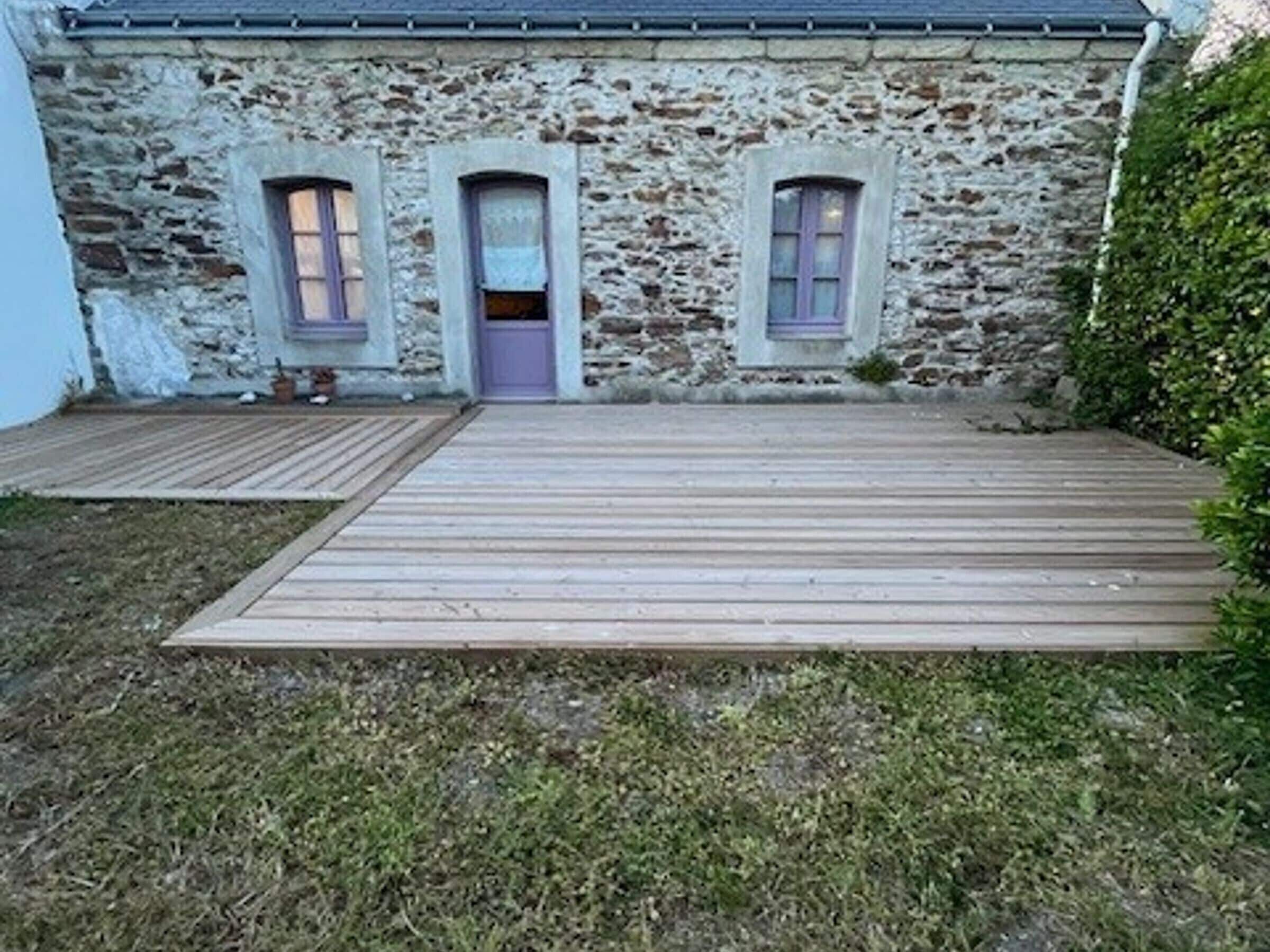 Ein Gebäude aus Stein mit einer Holzterrasse, drei Rundbogenfenstern und einer Tür.