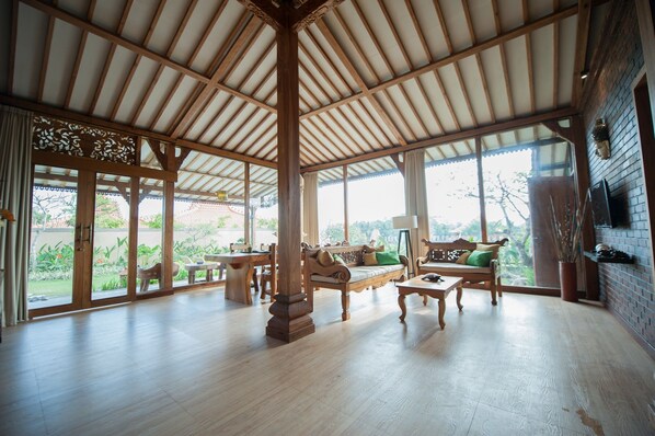 A spacious room with a high ceiling and large windows, wooden furniture, and a brick wall. - Apple Resort Retreat Spa (Tabanan)