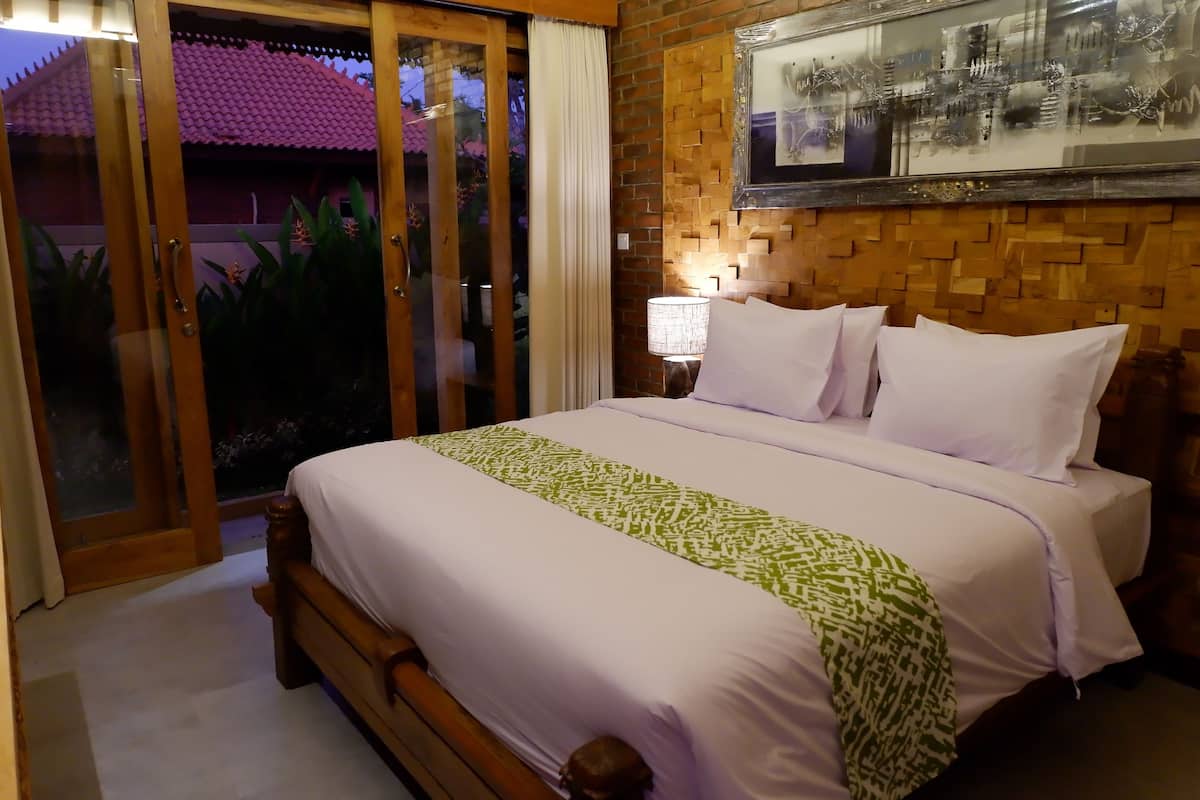 A bedroom with a bed, a nightstand, a lamp, and a wall-mounted picture.