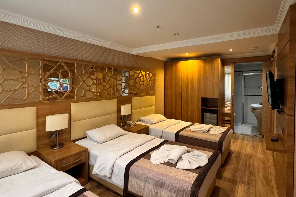 A hotel room with four beds, a wooden wall panel, a TV, and a bathroom visible through an open door.
