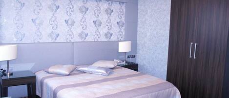 A hotel room with a large bed, two bedside tables with lamps, a wardrobe, and a patterned wallpaper.