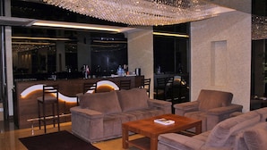 A modern lounge area with sofas, a wooden coffee table, and a bar with a neon light. - Prens Hotel (Istanbul)