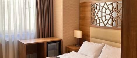 A hotel room with a bed, a desk, a lamp, and a decorative headboard.