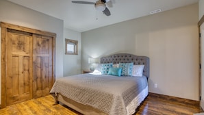 A bedroom with a large bed, wooden flooring, a ceiling fan, and a wooden door.
