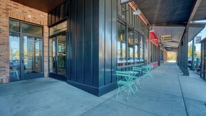 A building with a brick facade, large glass windows, and outdoor seating with green chairs.
