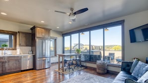 A modern kitchen with stainless steel appliances, a dining area with a table and chairs, and a large window offering a view of the outdoors.