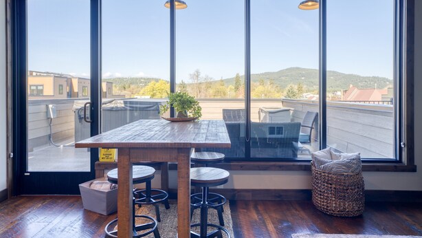 A modern room with a large window, a wooden table, and bar stools.