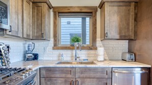 A kitchen with wooden cabinets, a stainless steel dishwasher, a built-in oven, and a window above the sink.