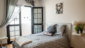 Een slaapkamer met een bed, een stoel, een nachtkastje met een lamp en een raam met gordijnen.