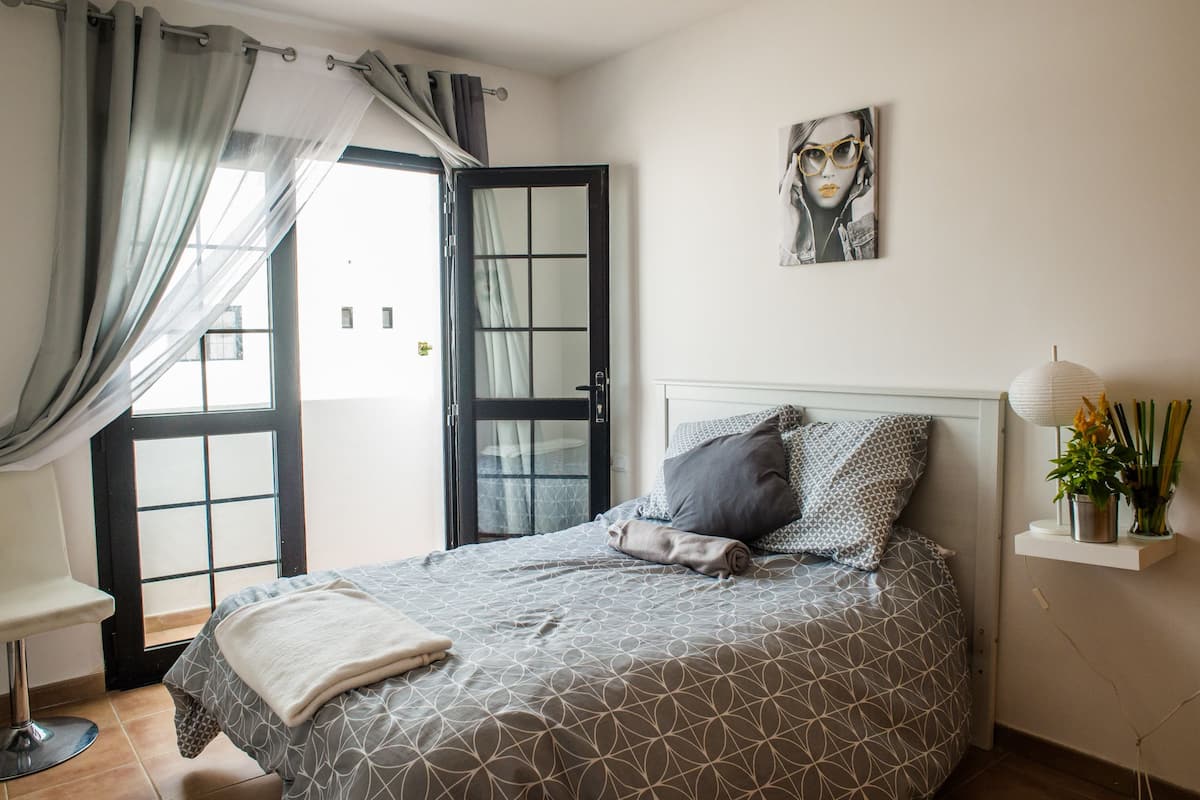 Une chambre à coucher avec un lit, une chaise, une table de chevet avec une lampe et une fenêtre avec des rideaux.